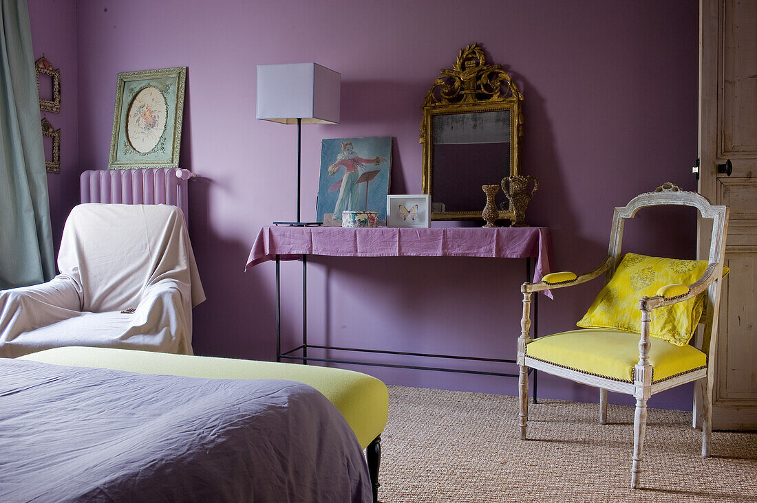 Schlafzimmer mit lila Wänden, goldgerahmtem Spiegel und gelbem Akzentstuhl