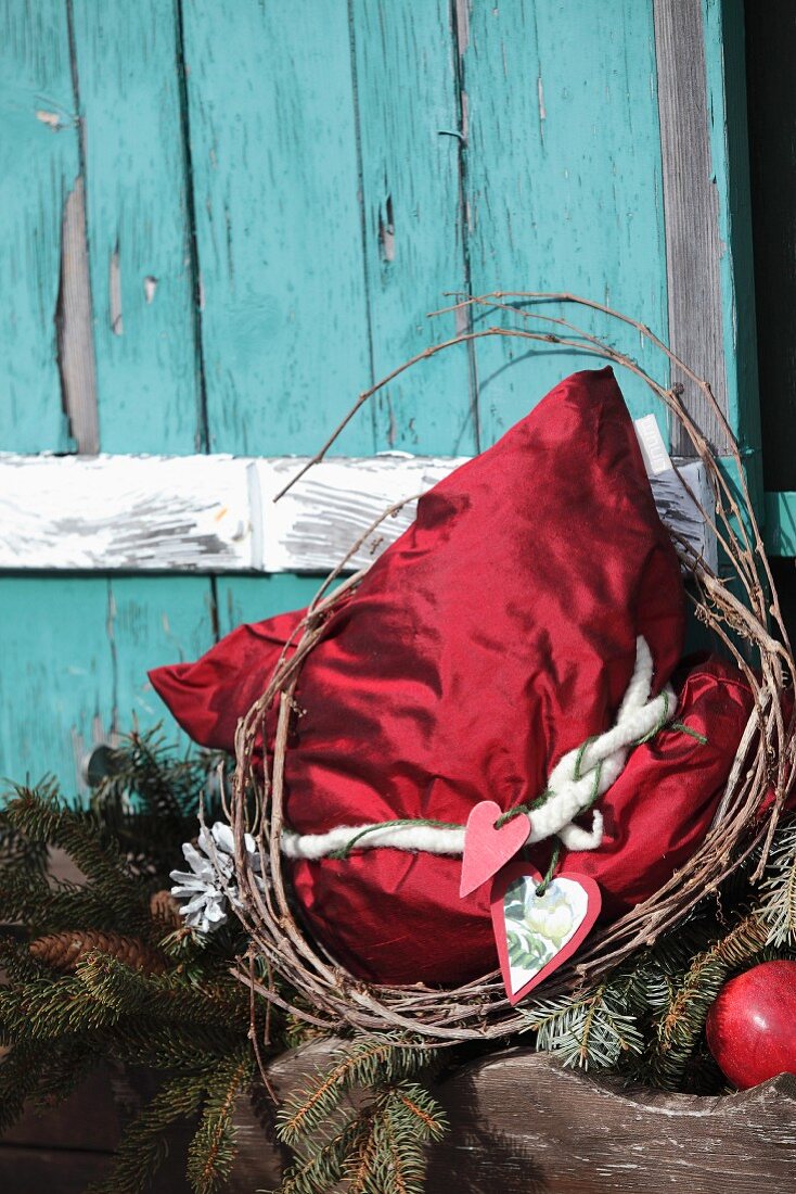 Rotes Seidenkissen mit nostalgischer Weihnachtsdeko vor türkisfarbenem Hütten-Fensterladen