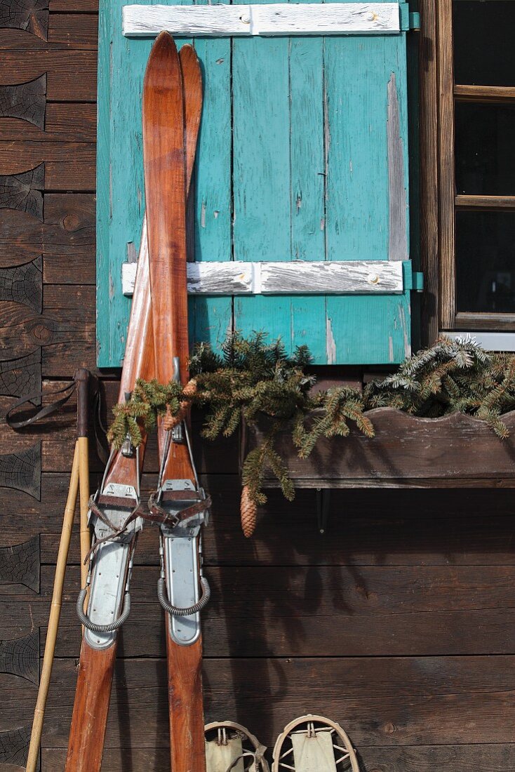 Vintage Skier an Hüttenwand und türkisfarbenem Fensterladen gelehnt