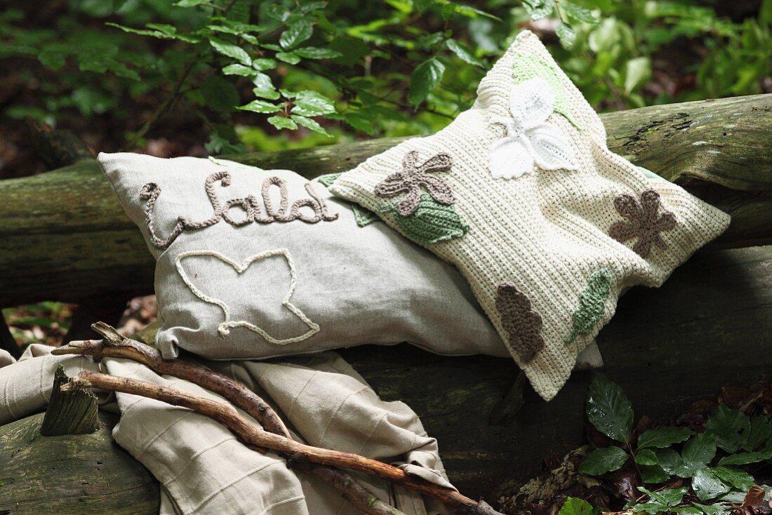 Various embroidered, crocheted and appliqué cushions on tree trunk in woodland