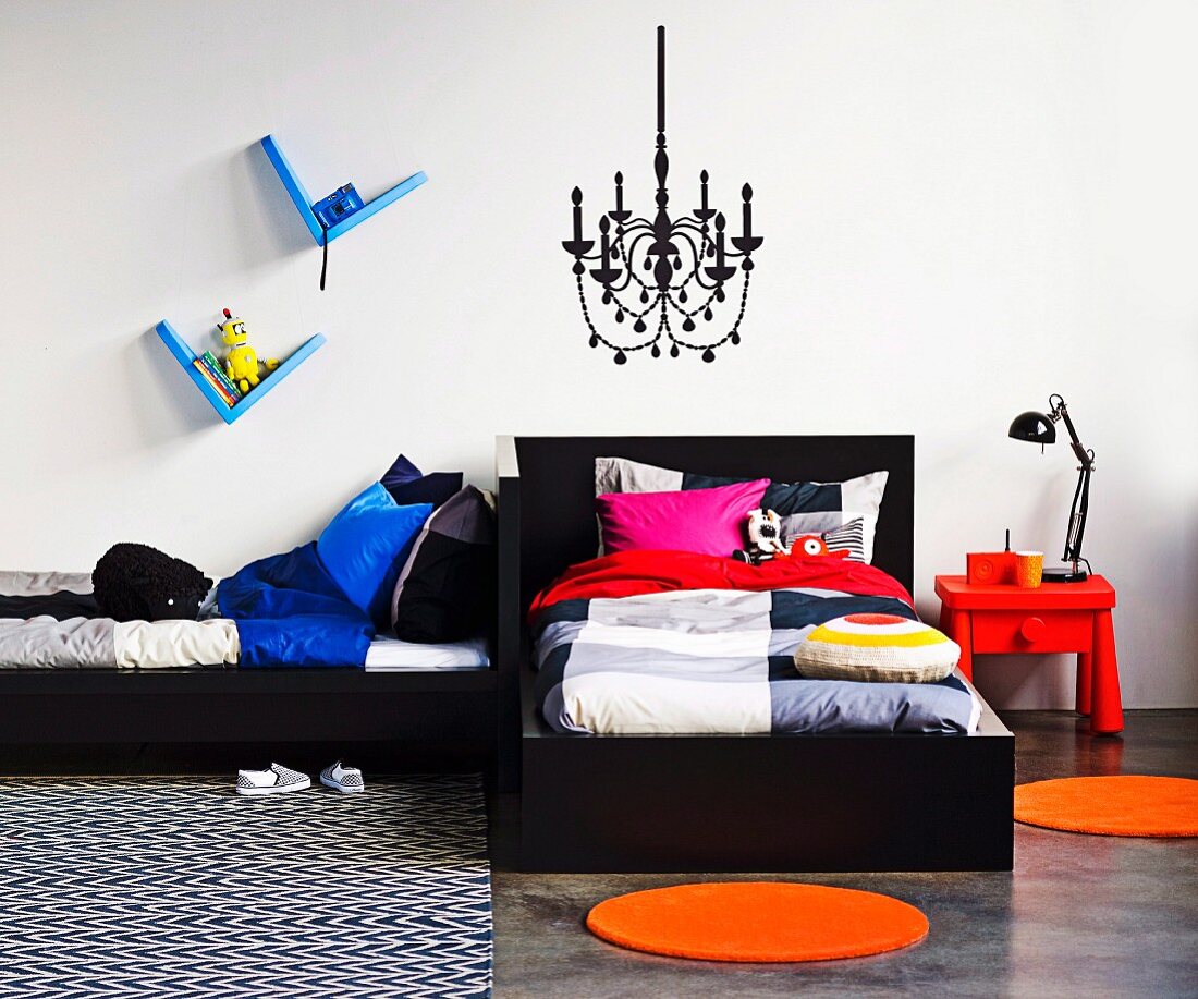 Twin beds arranged in an L in siblings' bedroom with chandelier painted on wall and colourful accessories