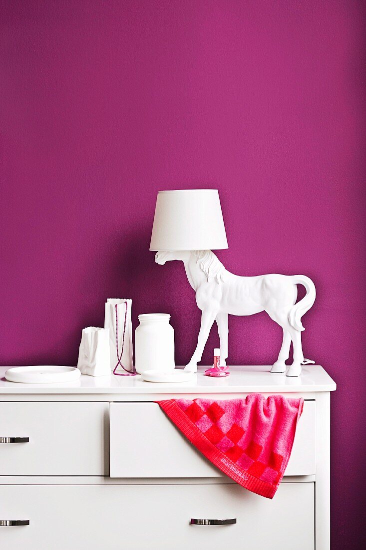 Accessoires im violett getönten Mädchenzimmer - Pferdefigur als Lampenfuss auf Kommode mit drapiertem Handtuchzipfel