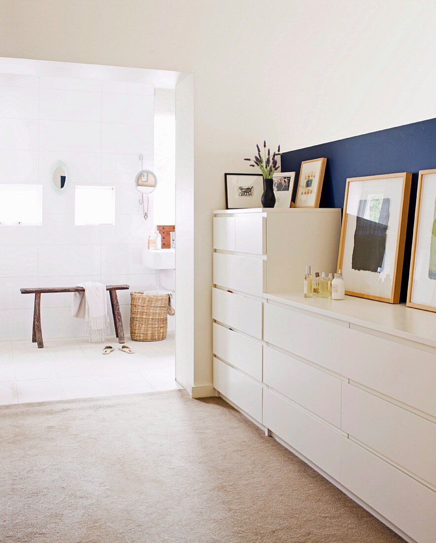 Dressing room with white chests of drawers leading to ensuite bathroom