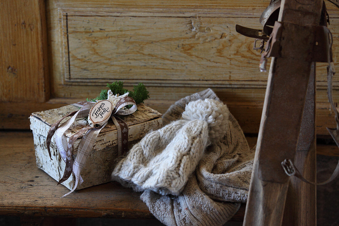 Knitted hat and gift in birch bark box on wooden bench next to vintage skis