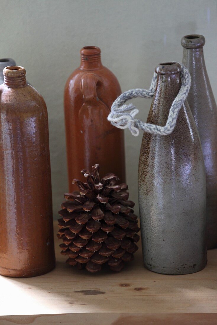 Vintage Keramikflaschen in Braun- und Grautönen und Kiefernzapfen