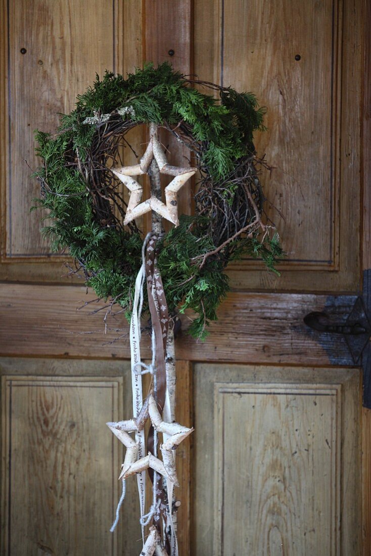 Kranz aus Thujazweigen, in der Mitte ein Stern aus Birkenzweigen mit Bändern, an rustikaler Holztür aufgehängt