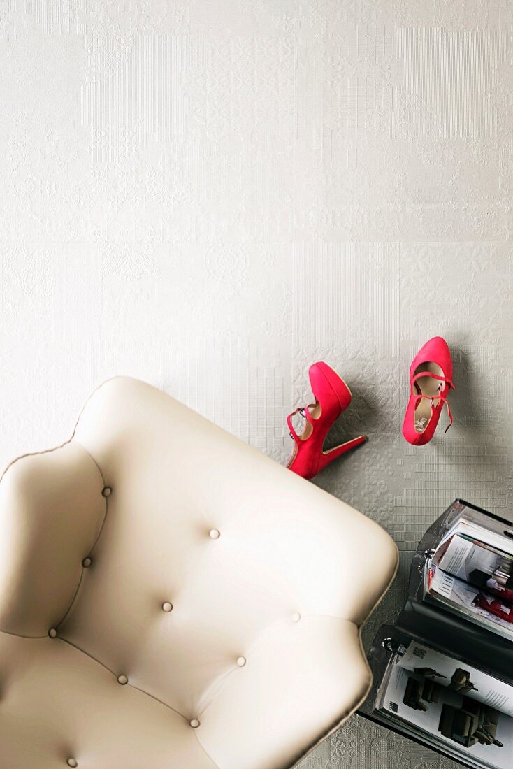 White, leather armchair, red ladies' shoes & magazine rack on white tiled floor with mixture of surface structures
