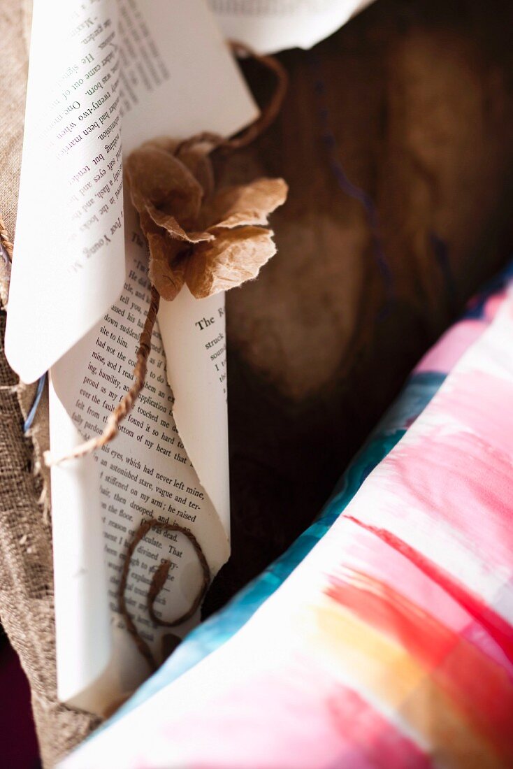 Pale brown paper flowers and rolled book pages next to patterned cushion