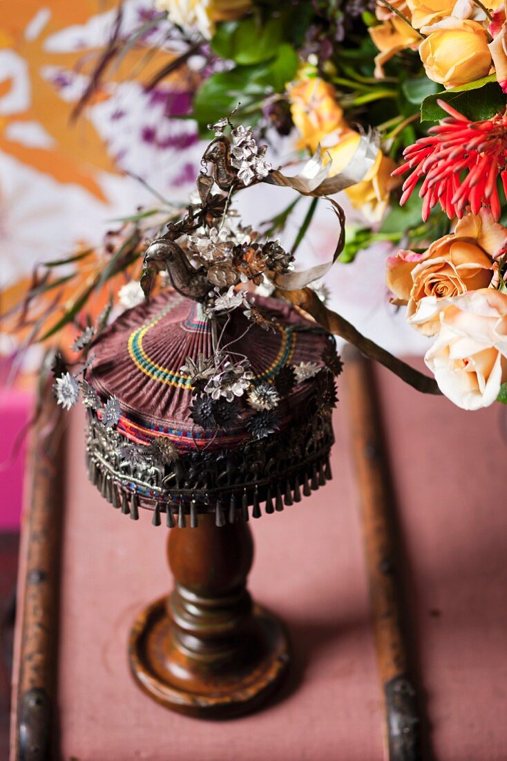 Folkloristische Tischleuchte mit Dekoblumen verziert neben teilweise sichtbarem Blumenstrauss