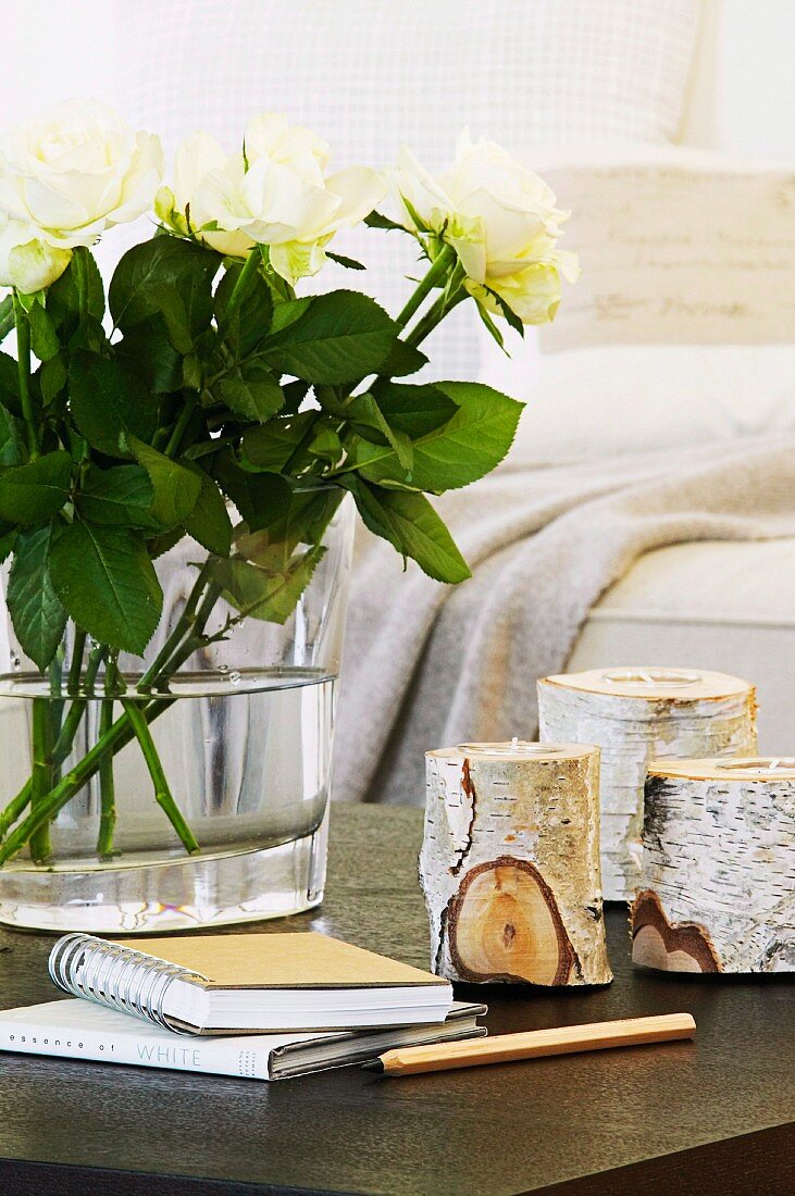 Tealight holders made from birch logs and white roses on table