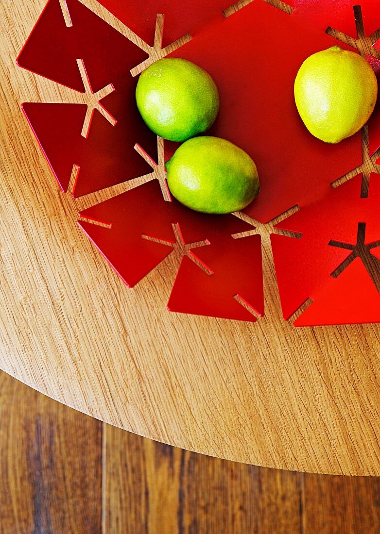 Zitronen auf roter Metallschale mit ausgestanztem Muster auf Holzuntergrund