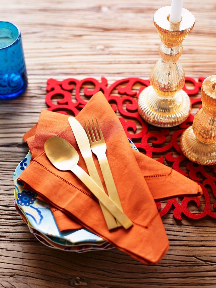 Farbenfrohe Tischdekoration mit rotem Tischläufer, goldfarbenen Kerzenleuchtern, orangefarbenen Stoffservietten auf rustikalem Holztisch