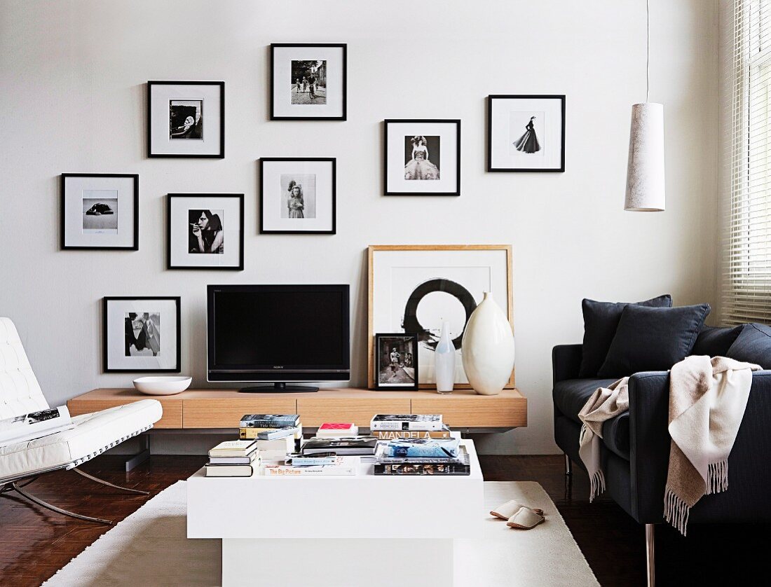Designer-TV-Möbel mit schwarzem Bildschirm umgeben mit verschiedenen schwarz-weiß-Aufnahmen in schwarzen Bilderrahmen an weißer Wand