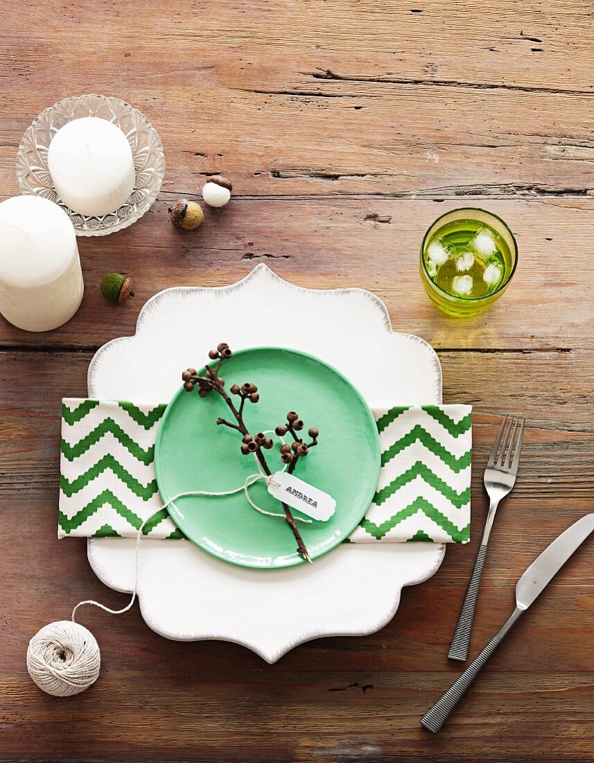 Geschwungener Teller mit grün-weißer Zickzackmuster-Serviette und lindgrünem Dessertteller auf rustikalem Holztisch mit Kerzen dekoriert