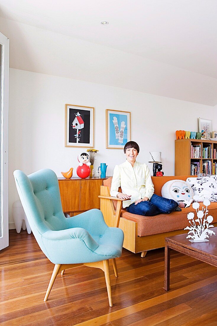 Classic pale blue armchair and woman sitting on sofa in living room with wooden floor