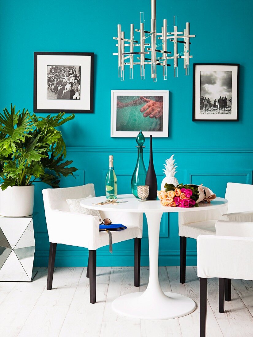 Replica designer lamp above small dining set; framed art prints on turquoise wall