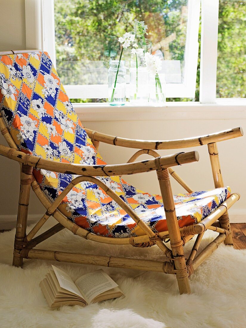 Sessel mit Bambusgestell und farbigem, gemustertem Polster am Fenster