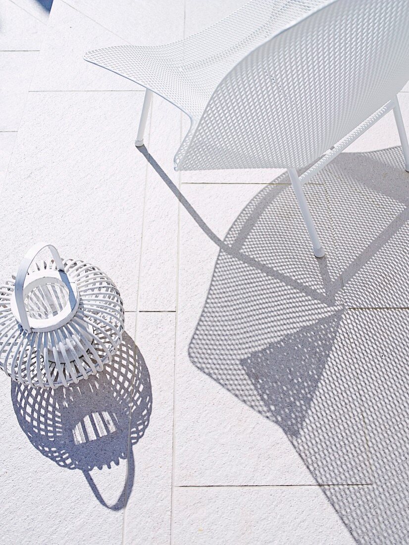 Schattenwurf von weißem Gitterstuhl und Korb-Windlicht auf hellen Bodenfliesen
