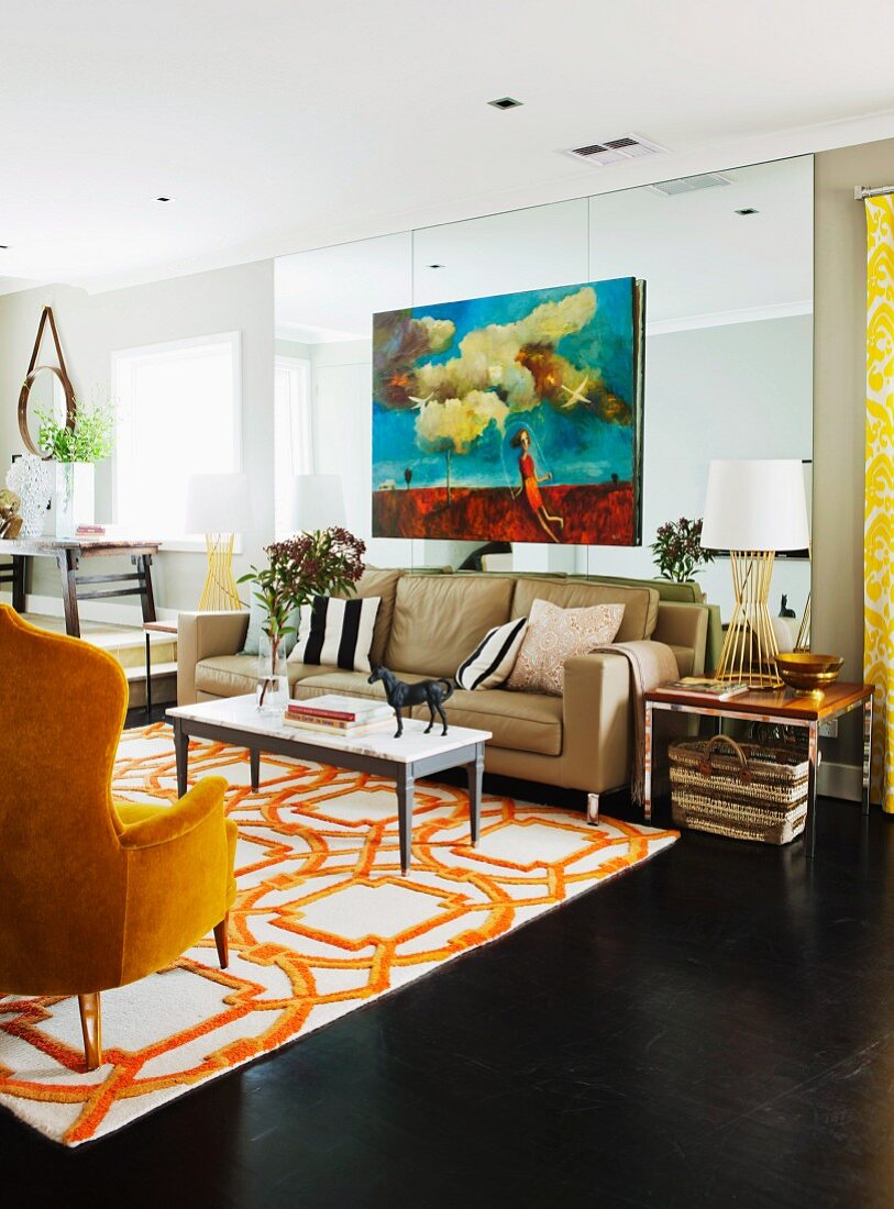 Loungebereich mit gelbem Lesesessel und Sofa um weissen Couchtisch auf weissorange gemustertem Teppich in offenem Wohnraum