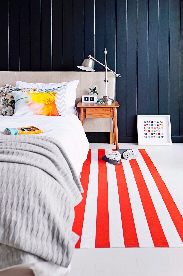 Schlafzimmer mit rotweiss-gestreiftem Teppichläufer vor schwarzer Holzverkleidung