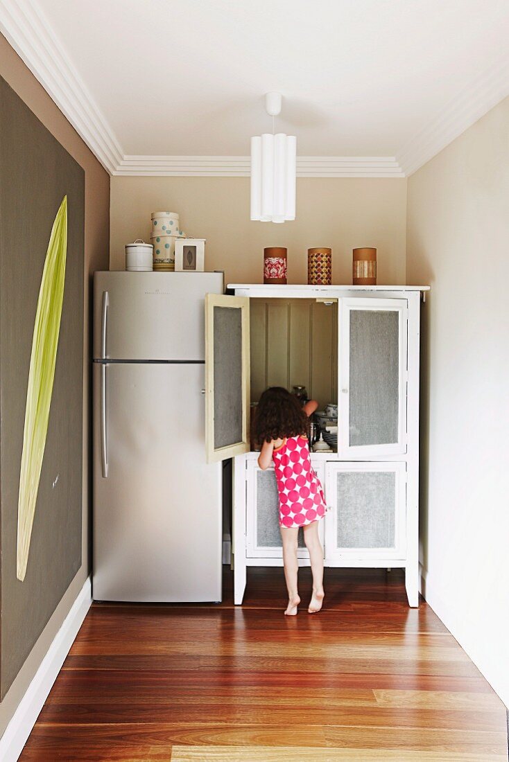 Kleines Mädchen an Geschirrschrank neben Kühlschrankkombination