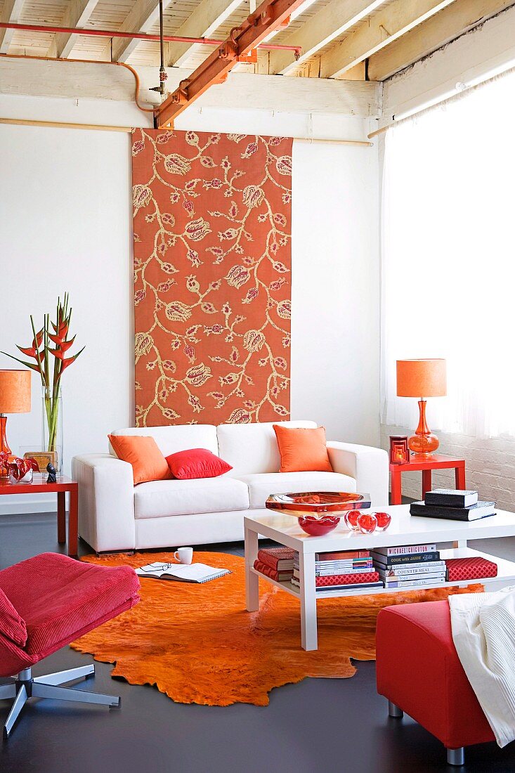 Wohnzimmer mit weiße Couchtisch auf orangem Teppich und grauem Linoleum Boden, weisses Polstersofa vor hochformatigem Stoffpaneel mit floralem Muster