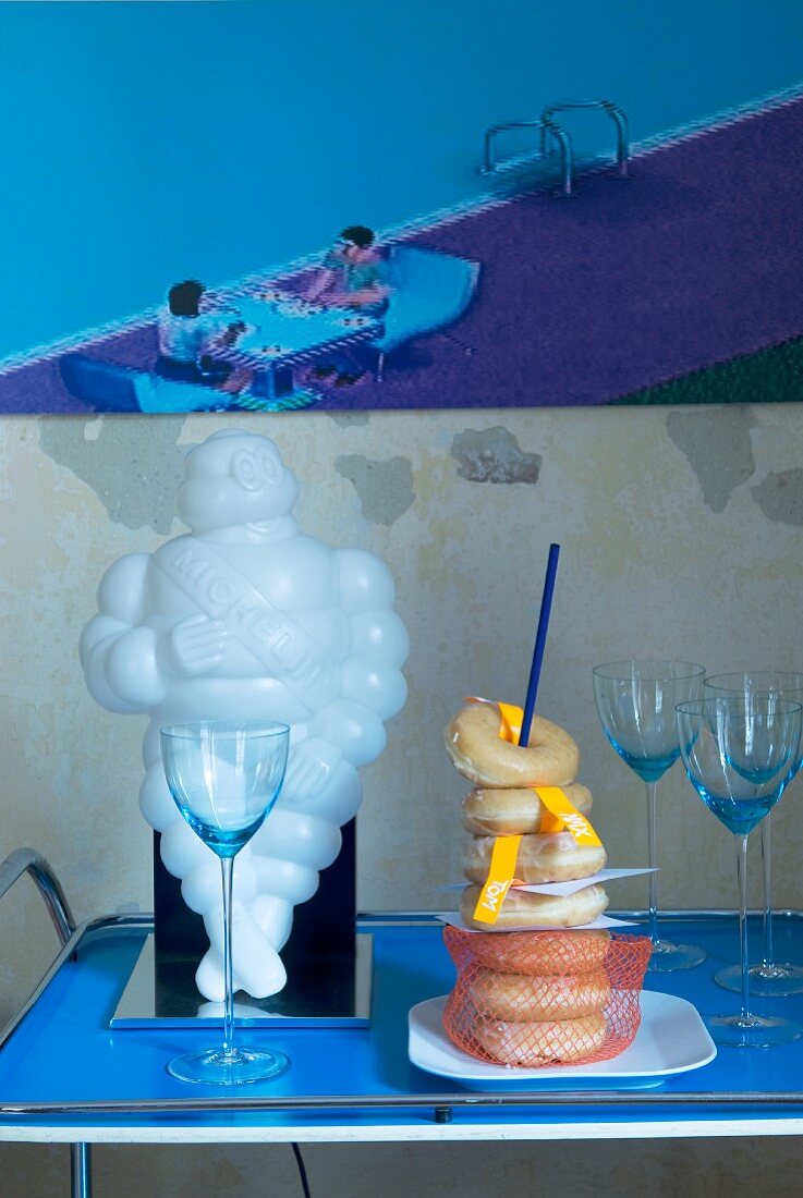 Retro Servierwagen mit weißer Michelin Männchen Figur, Donuts und Sektgläsern vor modernem Comuterbild in hellblau