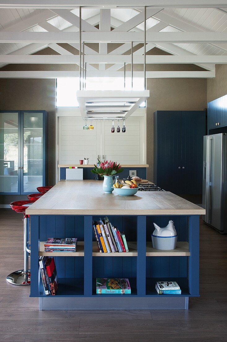 Large island counter with integrated, blue-painted shelves below ceiling lamp suspended from exposed roof structure