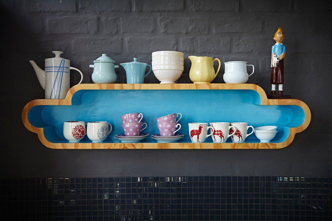 Nostalgic crockery on curved, pale blue, designer shelf on grey-painted grey wall