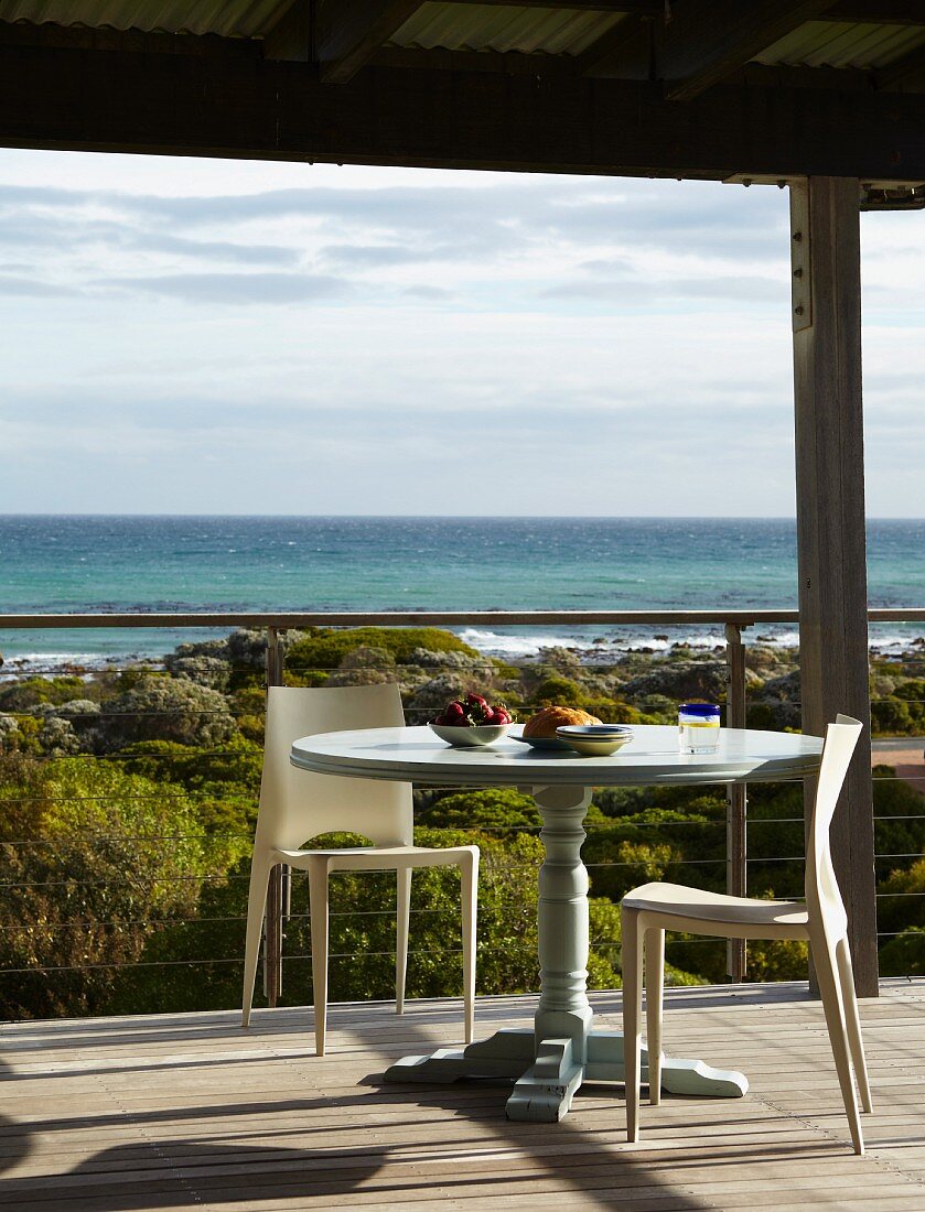 Zwei Designerstühle an rundem Vintagetisch auf überdachter Terrasse mit Blick auf das Meer