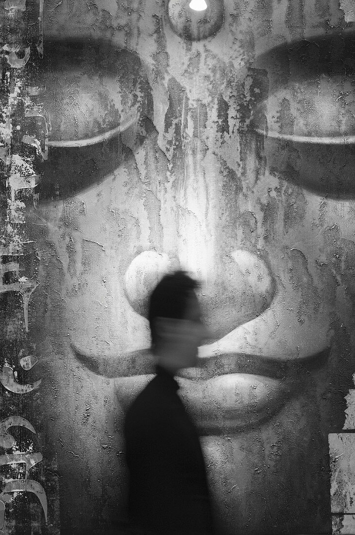 Grossformatige Schwarzweiss-Projektion eines Buddhagesichts; davor in Bewegungsunschärfe ein Mann im Profil