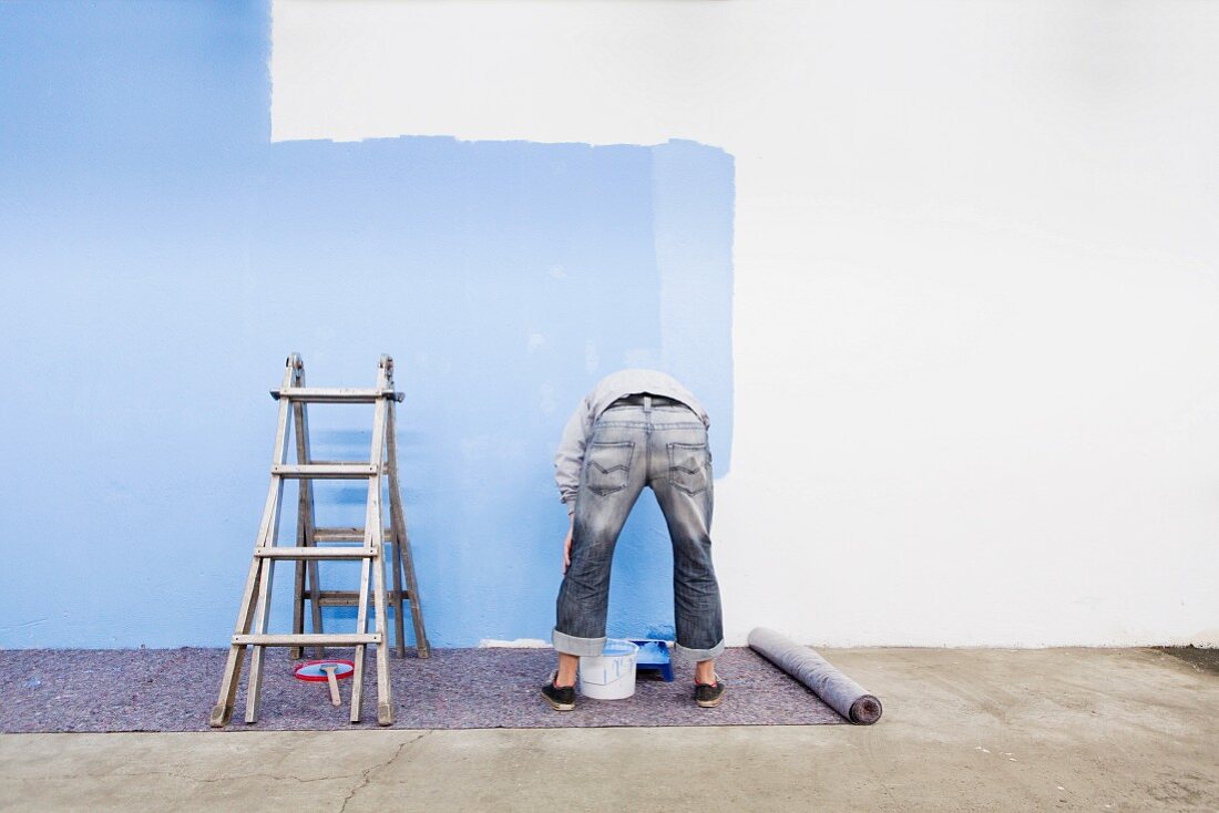 Mann streicht Wand mit blauer Farbe