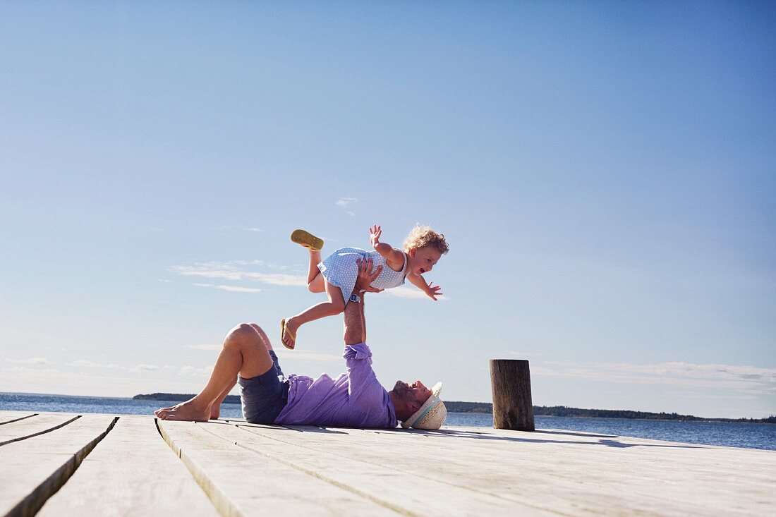 Father lying on a jetty and playing with his daughter