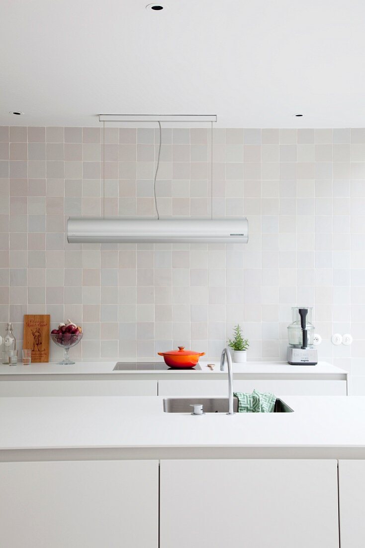 Reduzierte weiße Designerküche mit grau-weiß gefliester Wand und Designer-Arbeitsleuchte