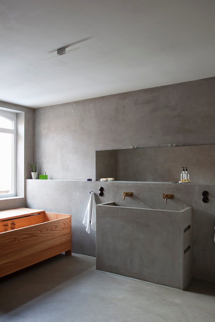 Designer, minimalist bathroom with wooden bathtub, concrete washstand and niche in concrete wall facing