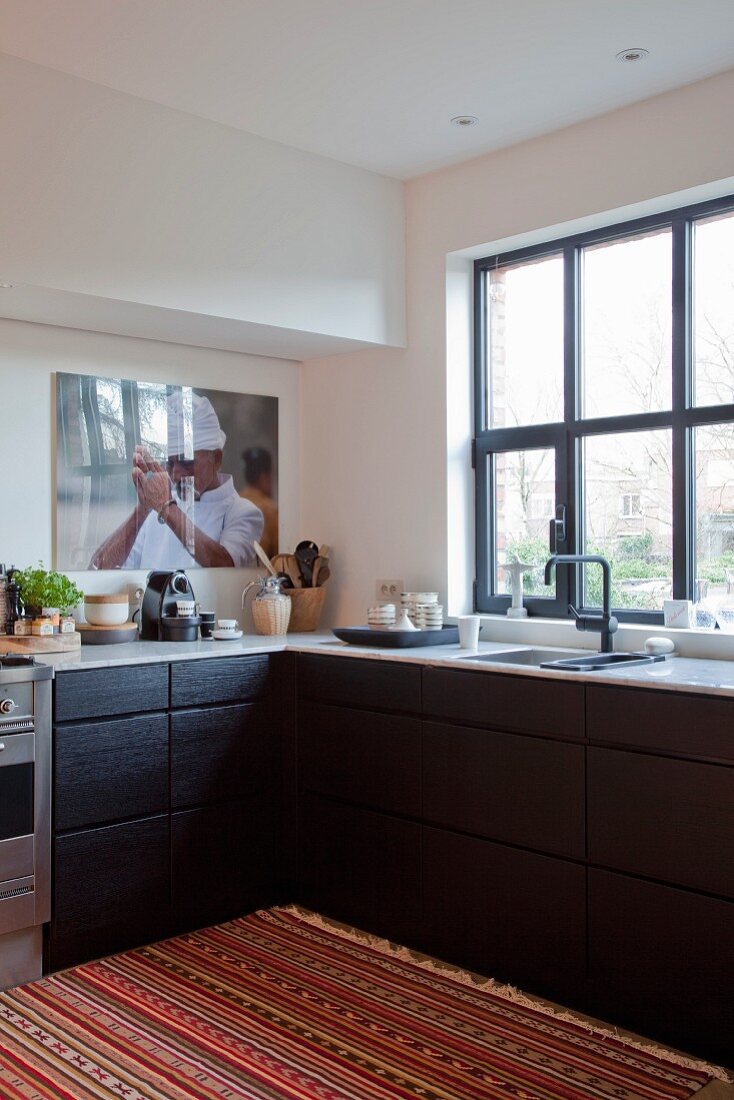Bunter gestreifter Teppich vor Küchenzeile übereck, schwarze Holzfront an Schubladenschränke in moderner Küche