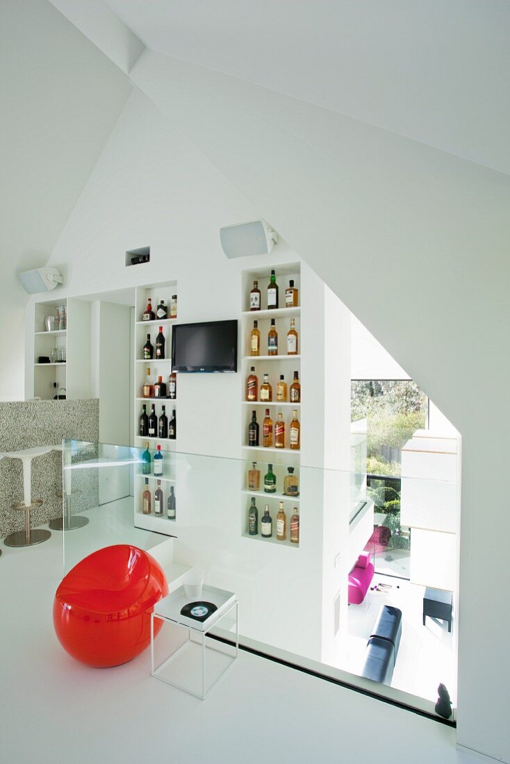 Mezzanine with collection of bottled on shelves, bar counter and view into ground-storey lounge area through glass balustrade