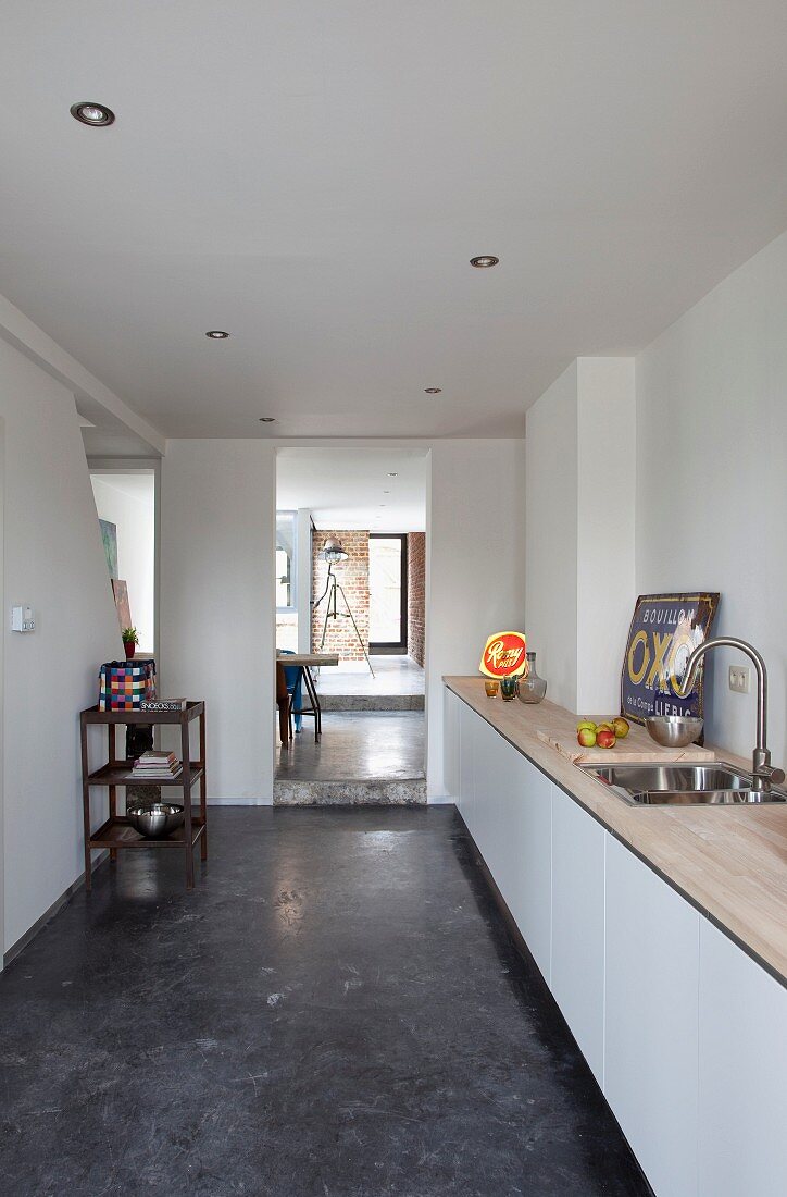 Minimalistischer Küchenbereich mit Küchenzeile und weissen Unterschränken, Blick durch raumhohen Durchgang in nachfolgende Räume mit unterschiedlich hohen Podesten