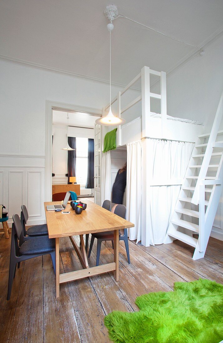 White-painted loft bed with ship ladder stairs, laptop on desk and green, faux fur rug on unpainted wooden floor
