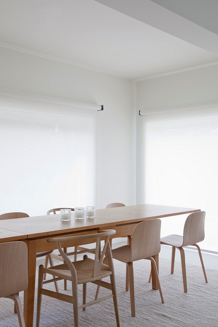 Langer Designer Holztisch mit Holzstühlen im skandinavischen Stil auf hellem Teppich vor Fenstern mit weißen transparenten Rollos
