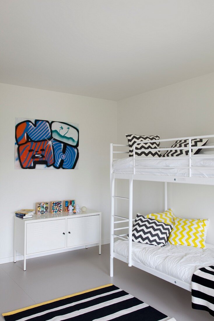 Children's bedroom with white bunk beds, scatter cushions with black and white zigzag patterns and striped rug