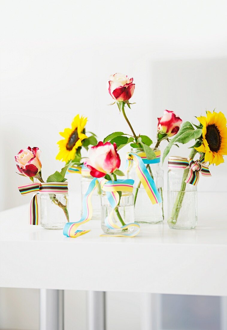 Single sunflowers and roses in glass vases decorated with ribbon