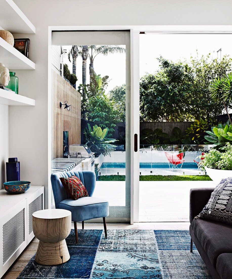 Blue retro armchair next to white built-in shelves and garden view with pool