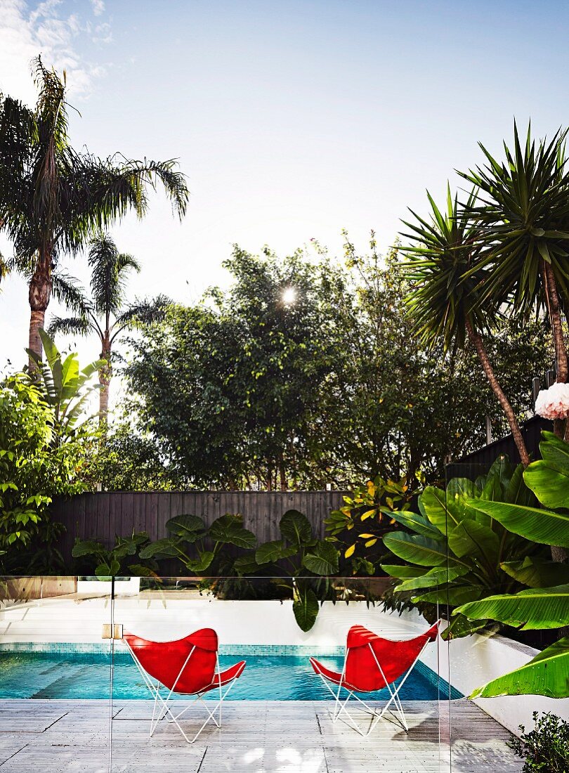 Pool mit zwei roten Butterfly Chairs hinter Glasbrüstung