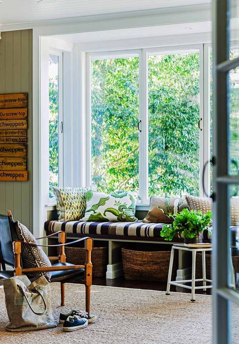 Sessel mit gespanntem Lederbezug in Schwarz und geschnitztem Holzgestell gegenüber Fensternische mit eingebauter Bank und Blick in Garten