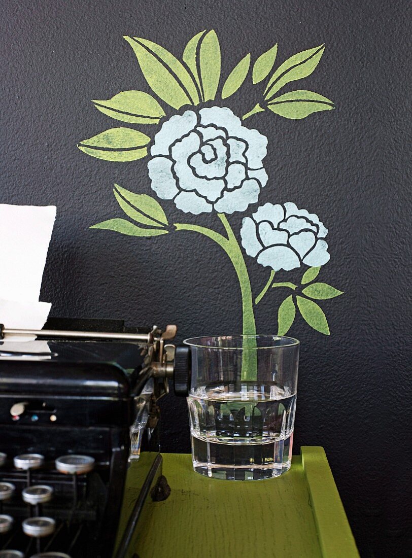 Wanddeko mit gemalter Blume & Wasserglas auf Wandtisch neben antiker Schreibmaschine