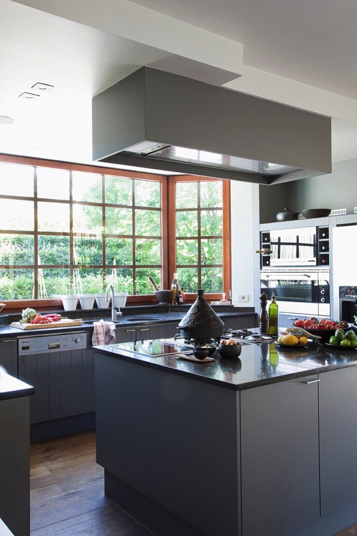 Food preparation on island counter with grey base units and kitchen counter below lattice window with view of garden