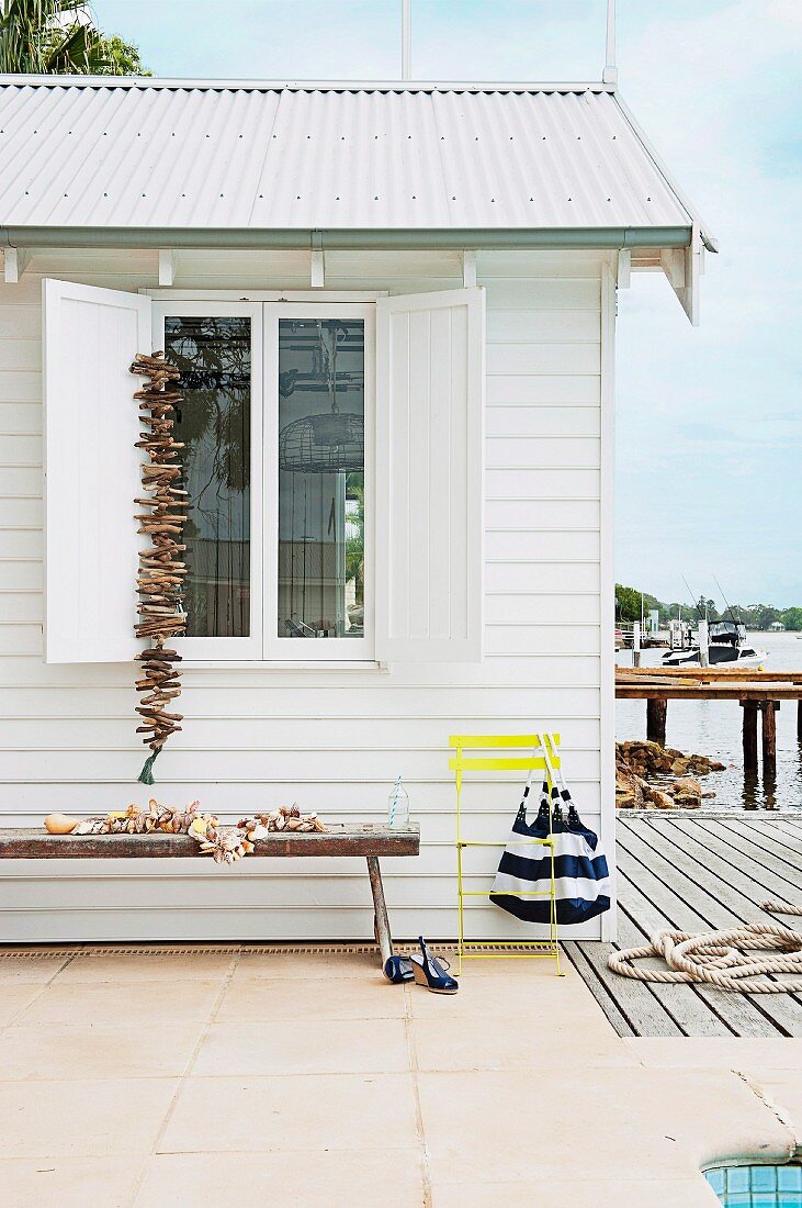 White beach cottage decorated with shells and drift wood; a long wooden bench along the side of the wall