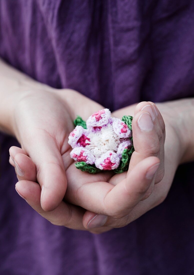 Liebevolle Geste mit in Händen gehaltener Häkelblüte