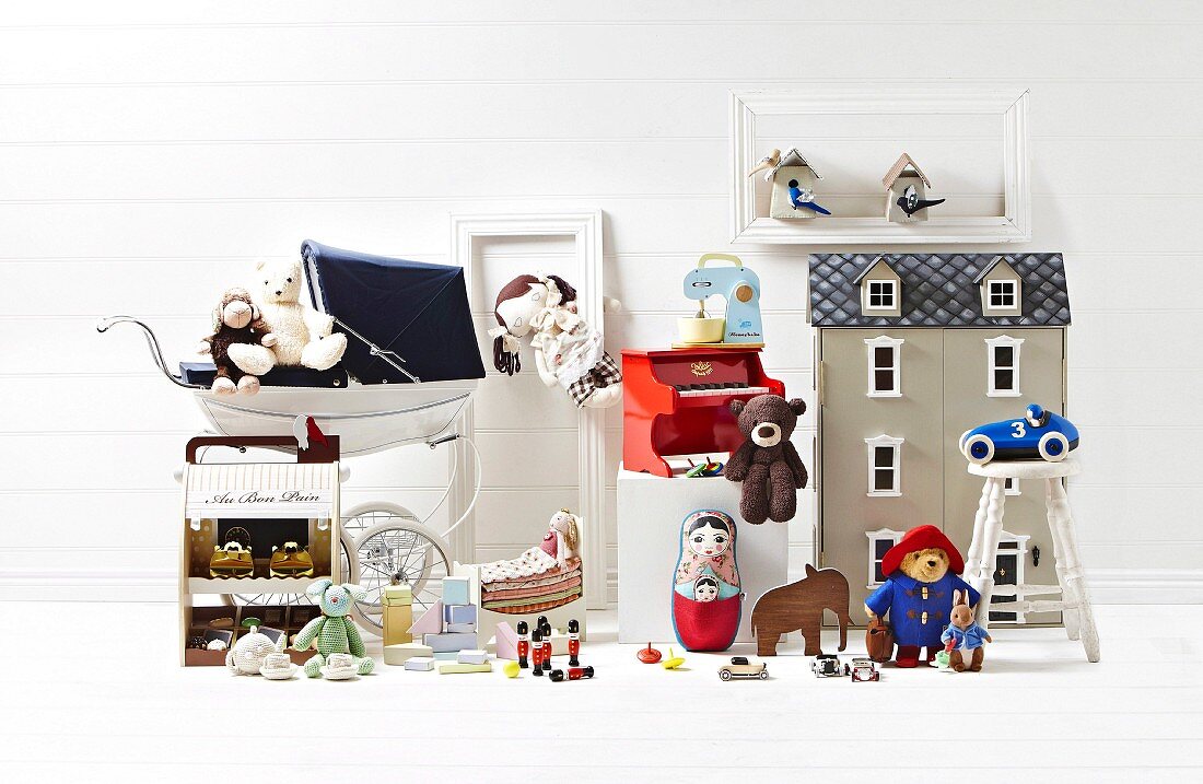 Spielzeug-Stillleben mit grauem Puppenhaus und nostalgischem Puppenkinderwagen